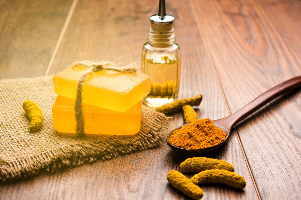Turmeric essential oil with soap and dried Haldi sticks and powder in a wooden spoon