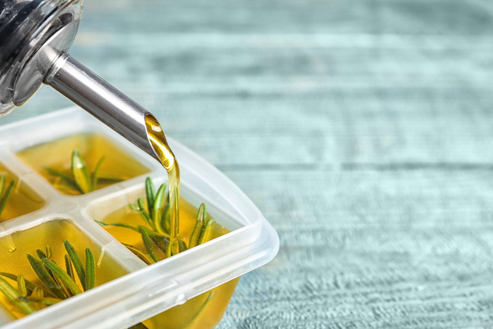 Pouring olive oil on rosemary in ice cube tray